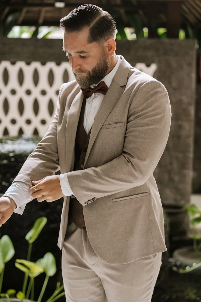 Close-up of groom adjusting his cuff wearing a tan suit with a brown tweed vest and bow tie.