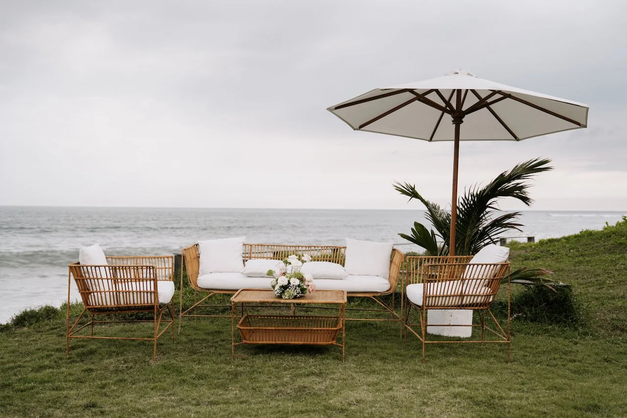 Rattan outdoor lounge furniture setup on a grassy cliff overlooking the ocean.