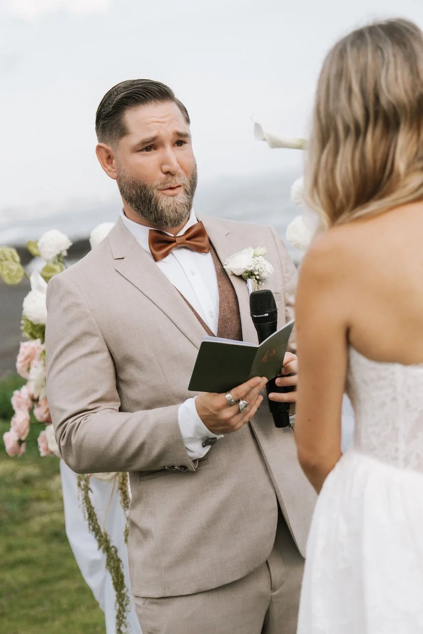 Groom reading heartfelt wedding vows from a dark green custom booklet at the altar.