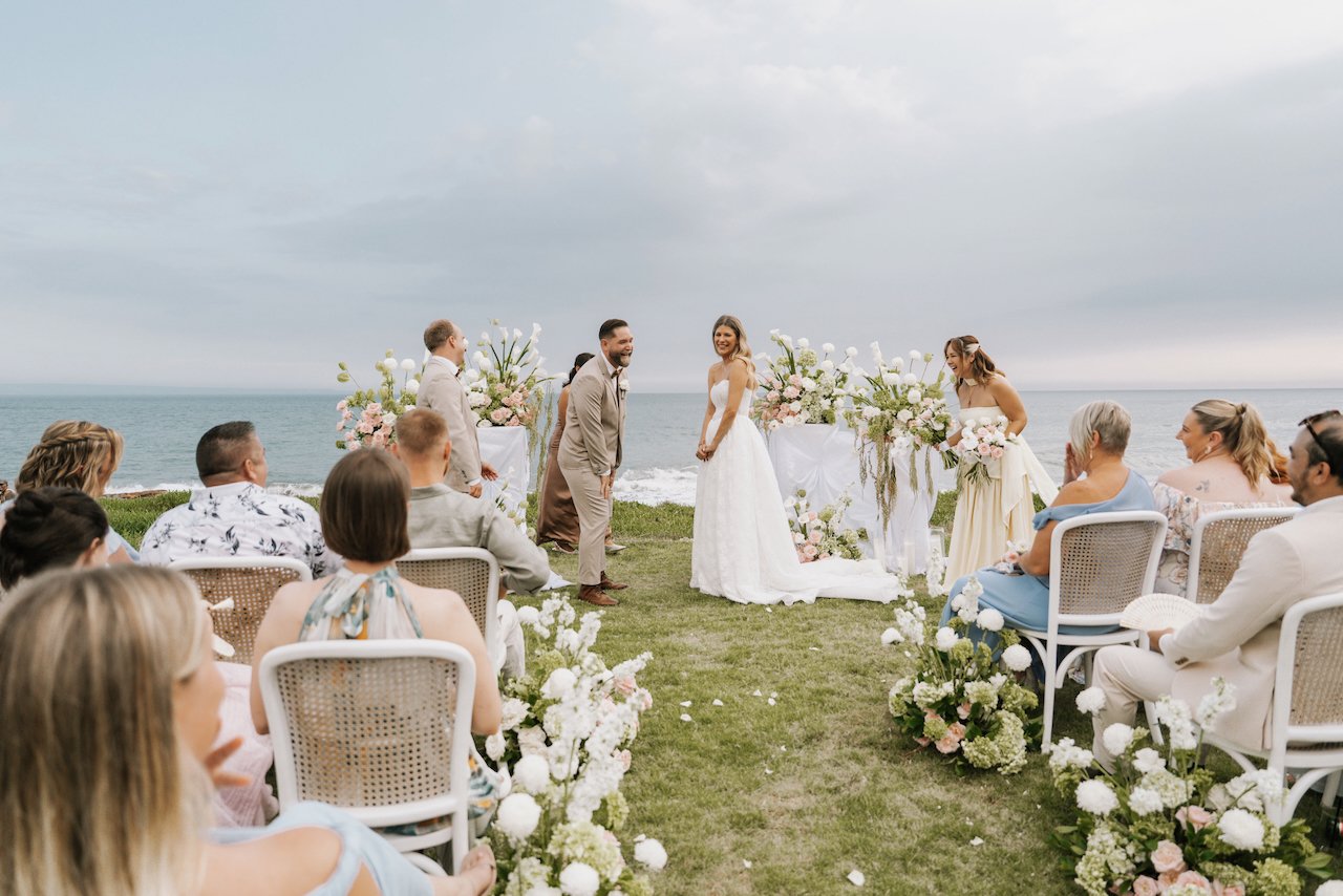 Bride and groom sharing a laugh at the altar surrounded by lush white floral arrangements.
