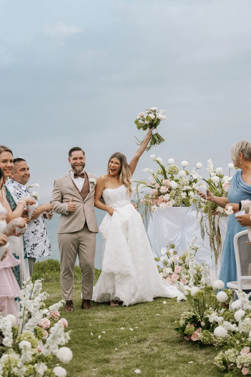 Excited bride raising her floral bouquet while walking up the aisle with her new husband.