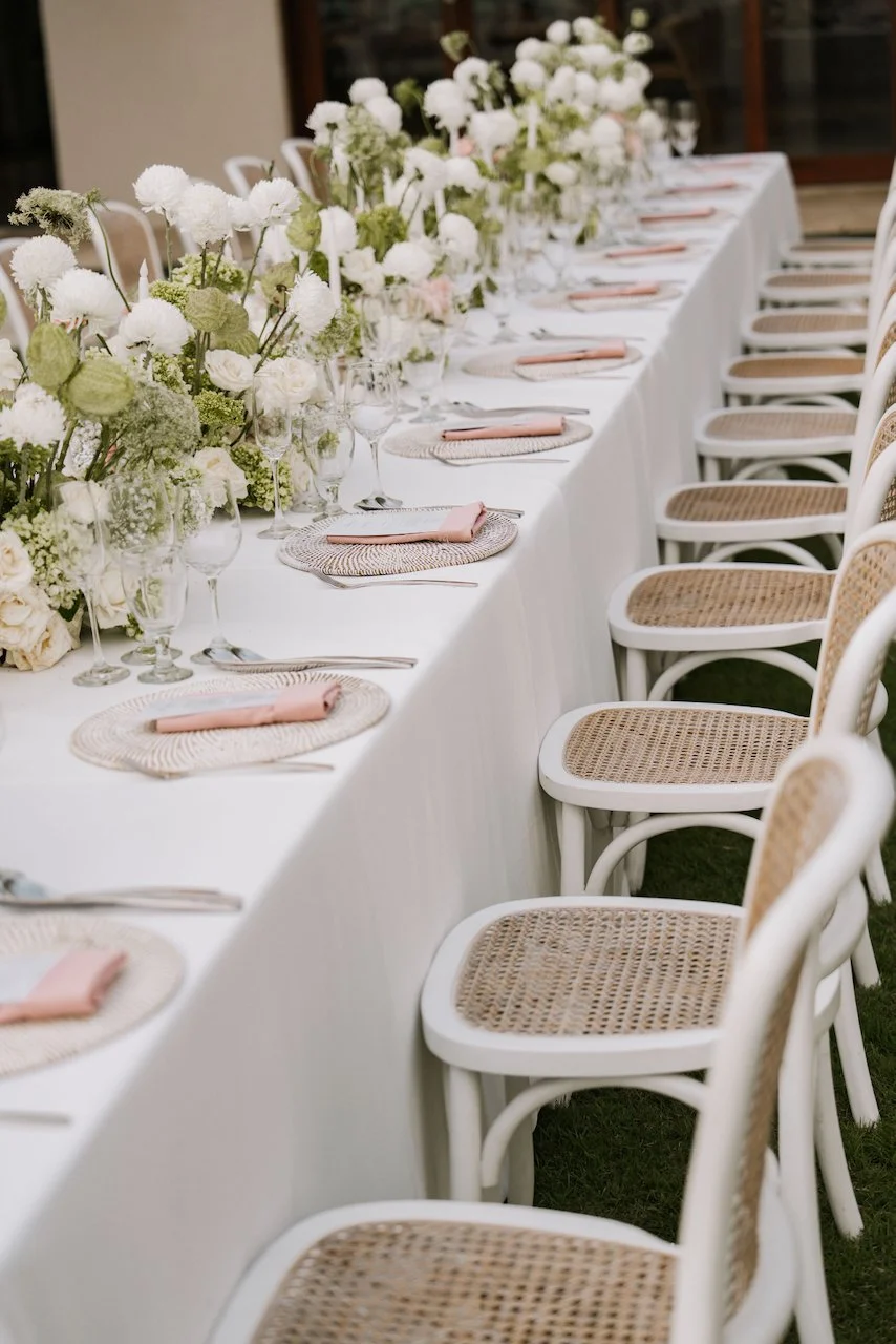 Close-up of tropical reception table decor with woven placemats, pastel pink napkins, and white florals.