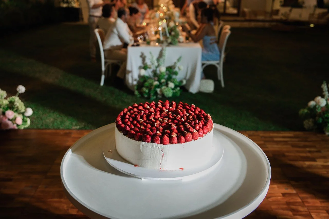 Single-tier white wedding cake completely covered in fresh strawberries displayed outdoors.