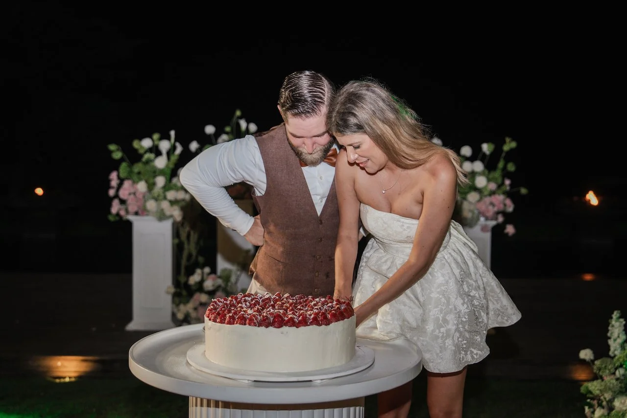 Bride in a short white reception dress and groom cutting their strawberry wedding cake together.