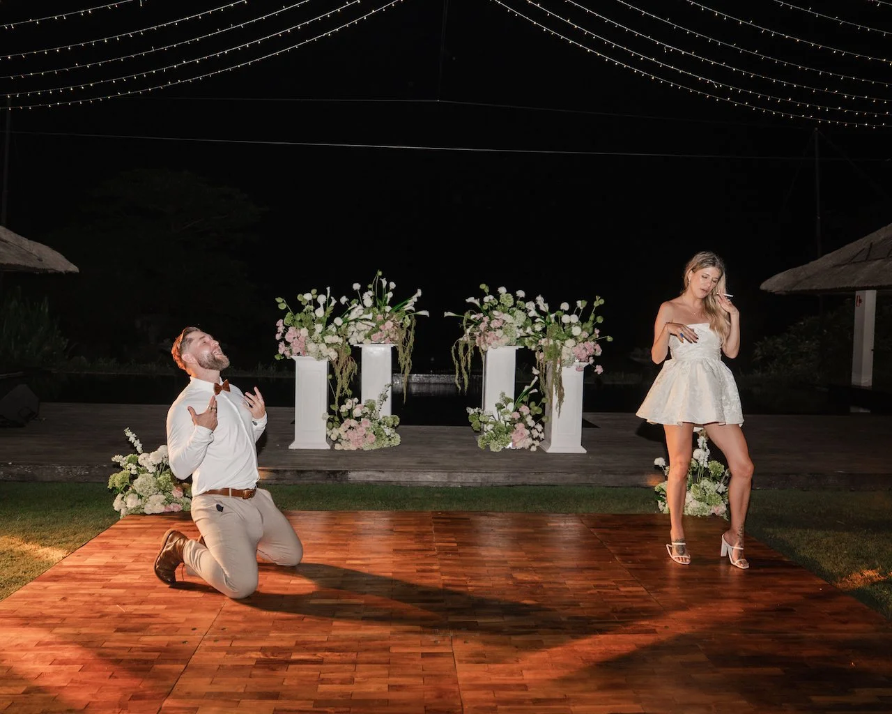 Playful groom on his knees on the dance floor while the bride stands nearby during the wedding afterparty.