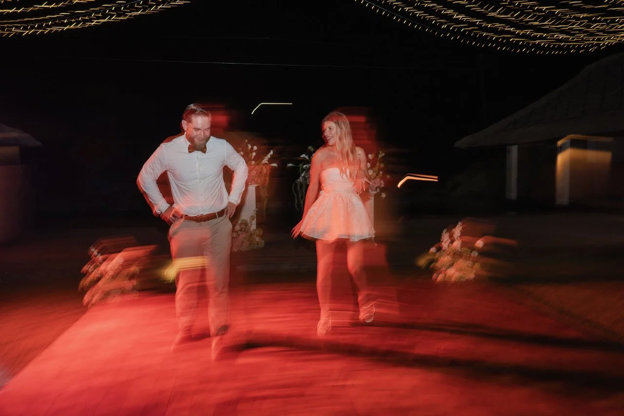 Creative motion blur photography of the newlywed couple smiling and dancing on an outdoor wooden floor.