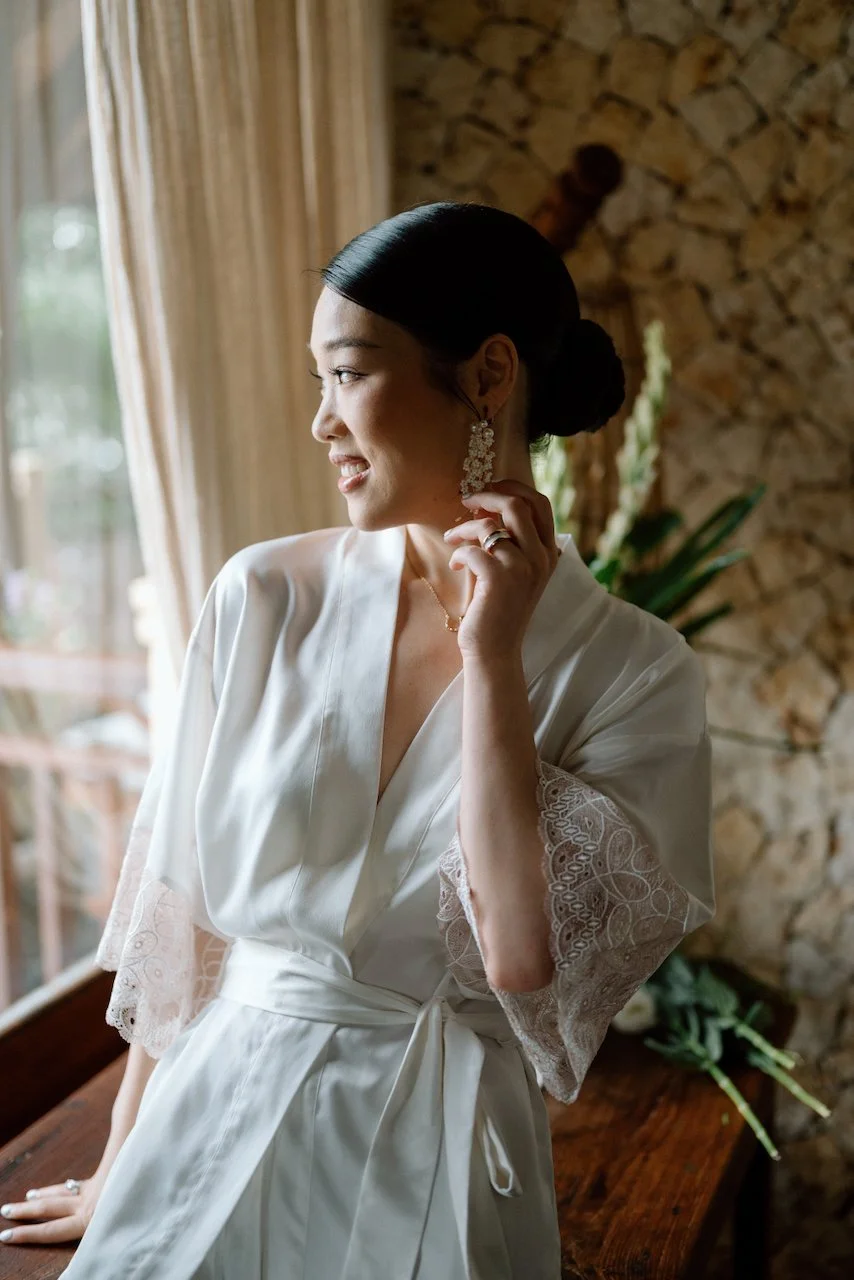 Silver Lace Weddings bride adjusting an earring in a silk getting-ready robe.