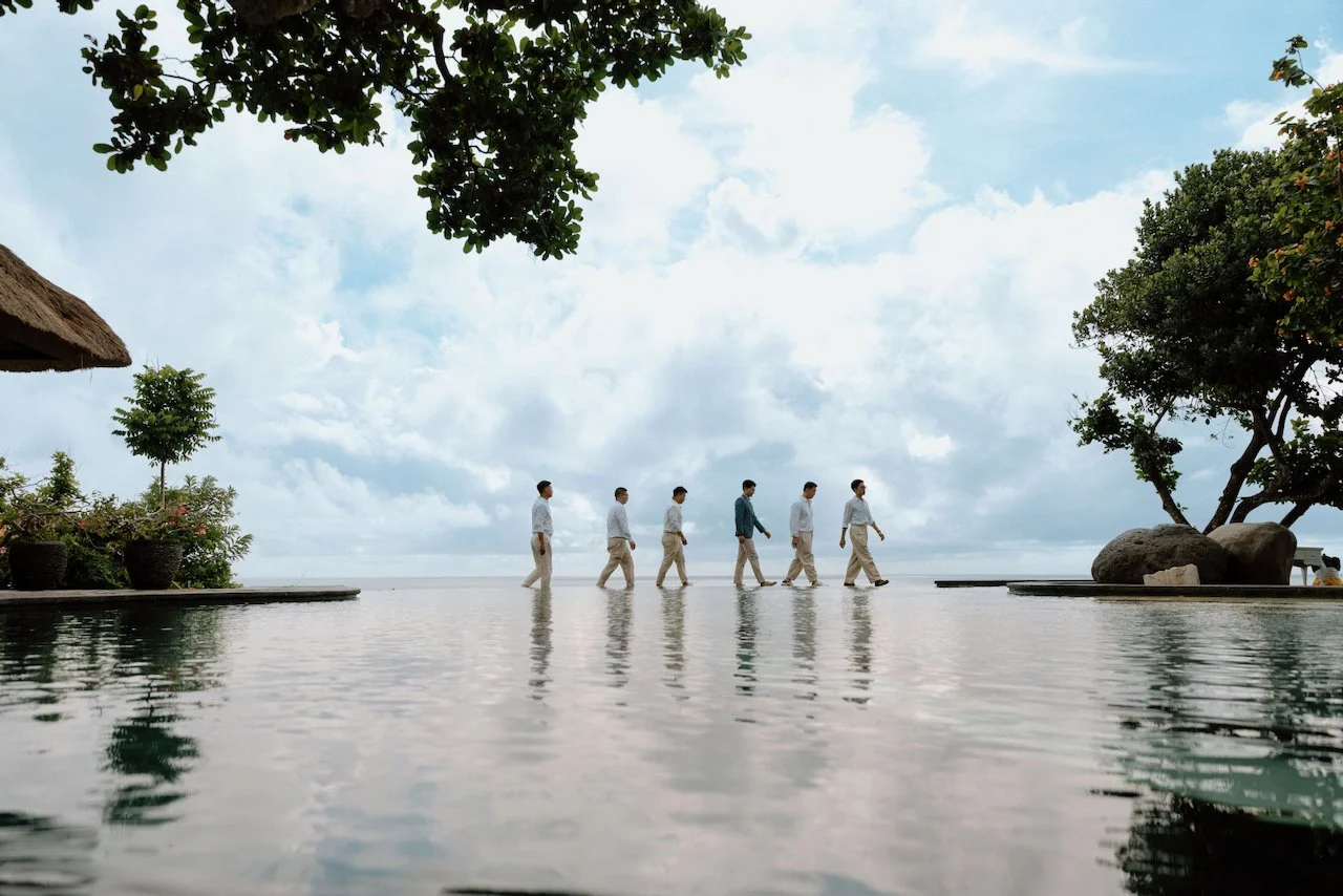 Groomsmen walking along a cliffside infinity pool edge in Bali.