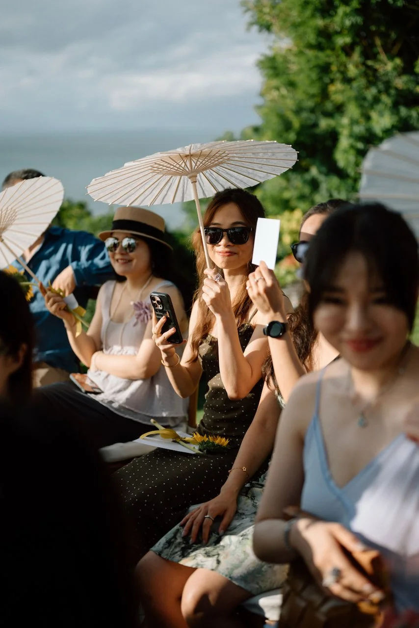 Guests staying cool under parasols at a sunny outdoor ceremony.