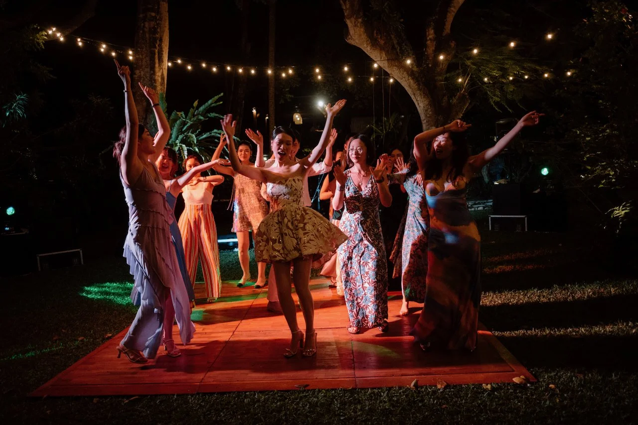 Wedding party dancing enthusiastically under string lights in the jungle.