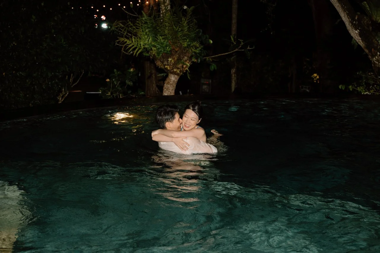 Bride and groom sharing a playful kiss in a Bali swimming pool at night.
