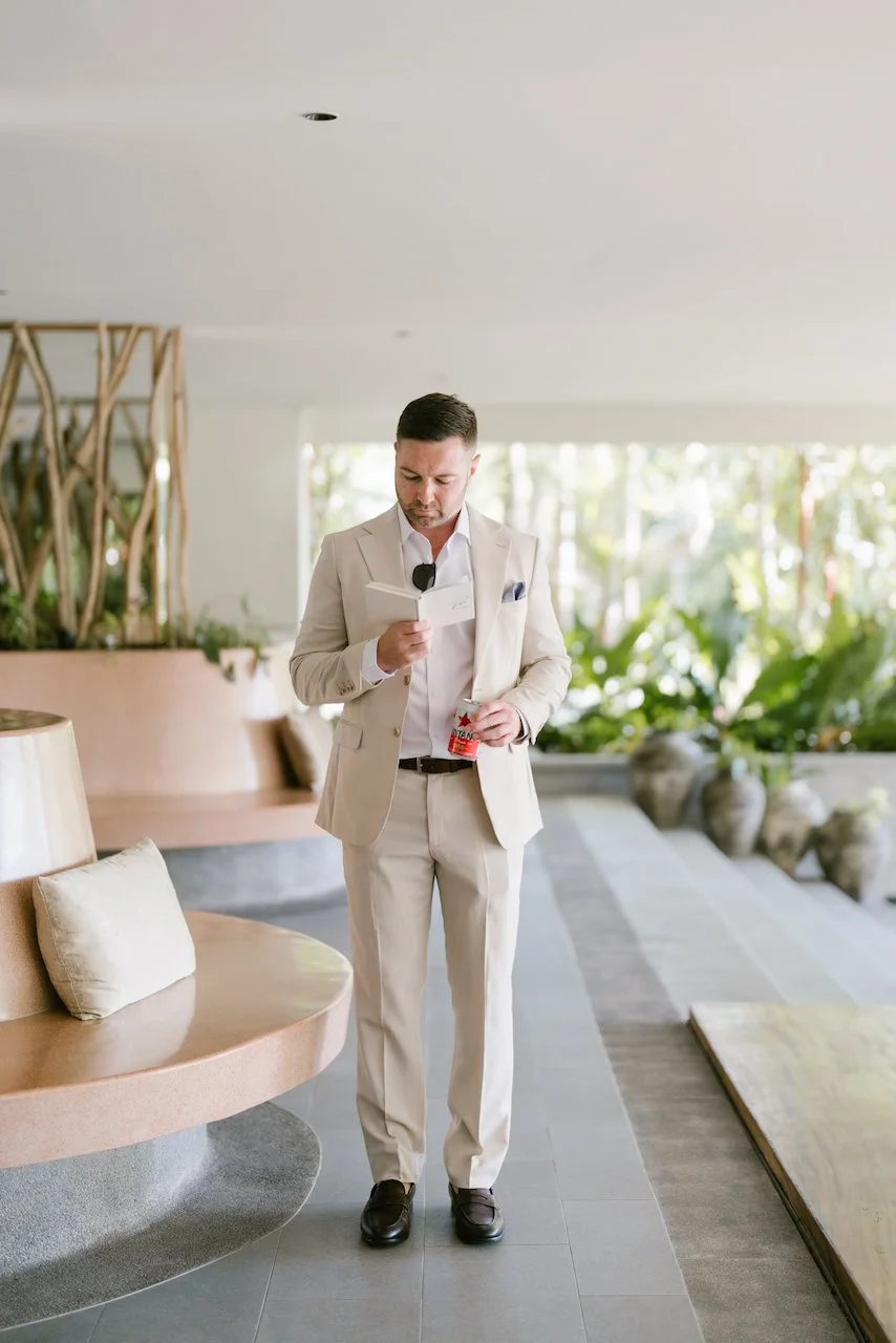 Groom Thomas wearing a tailored beige suit standing in a modern resort suite