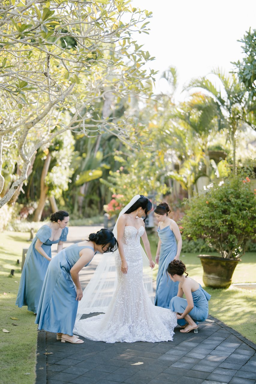 Bridesmaids in blue dresses helping the bride adjust her wedding dress train outdoors