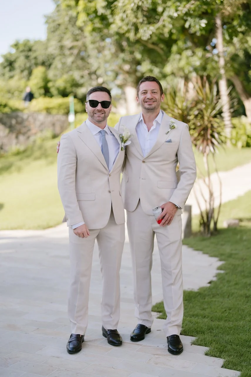 Groom and groomsman in matching tan suits posing on the tropical grounds of Ayana Bali
