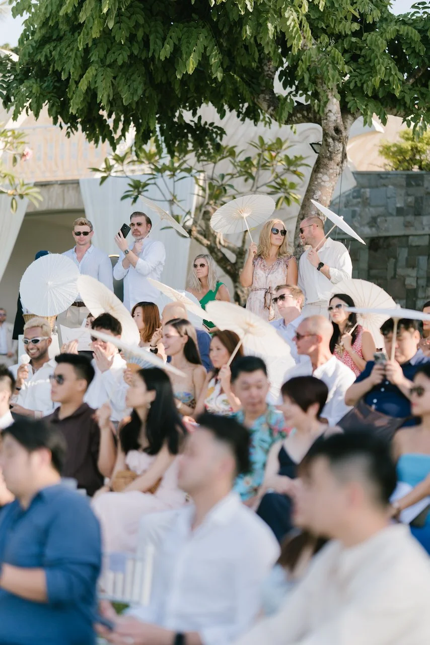 Wedding guests seated outdoors under tropical trees during the ceremony at Ayana