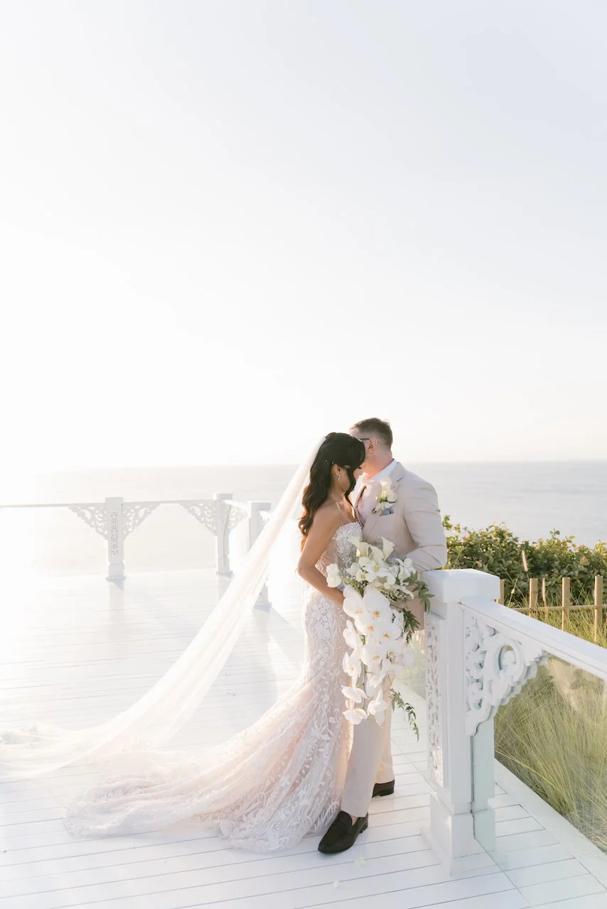Bride and groom embracing on a scenic white architectural bridge overlooking the ocean