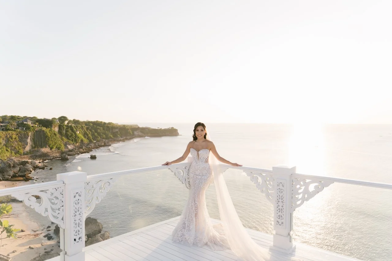 Bride Zoe posing solo on a white oceanfront bridge at sunset showcasing her bridal train