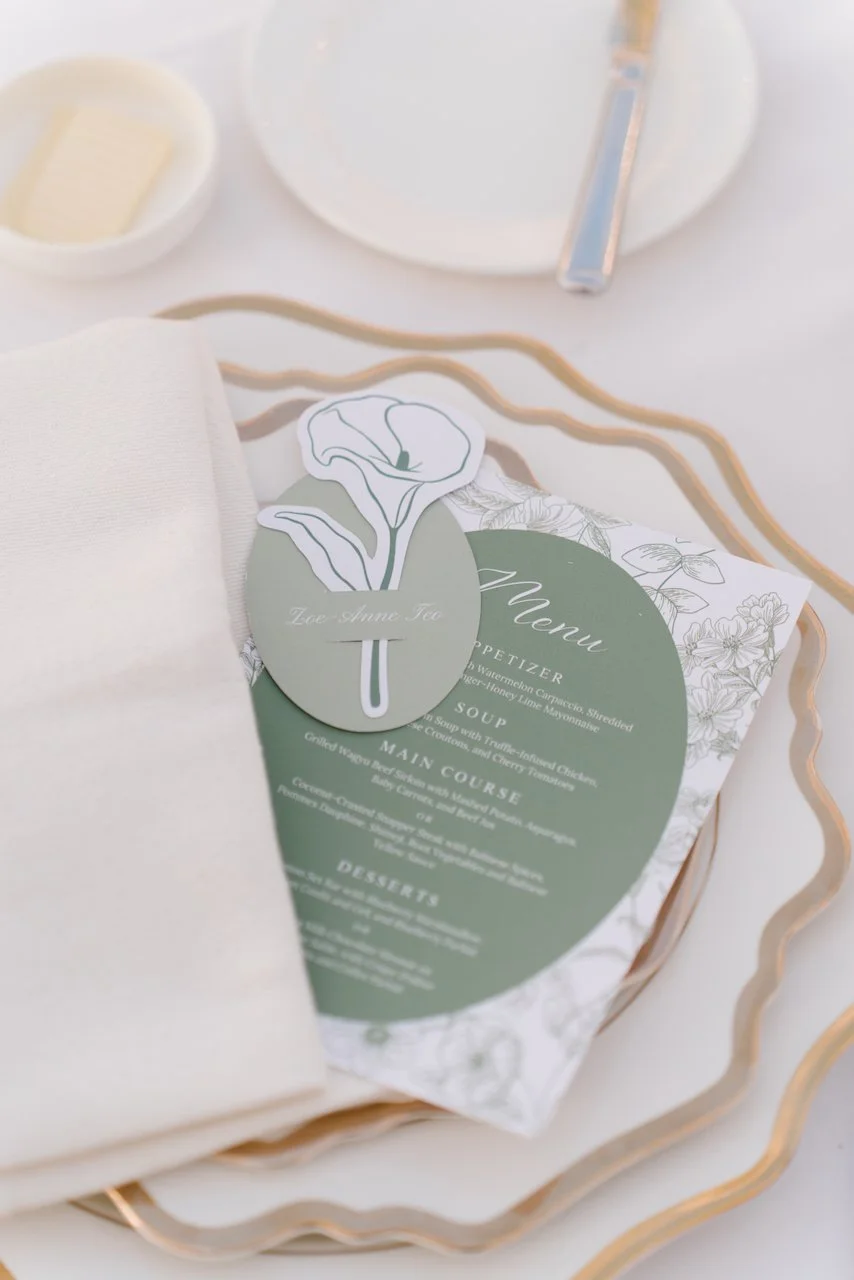 Close-up of a custom green menu card and white textured charger plate on a reception table