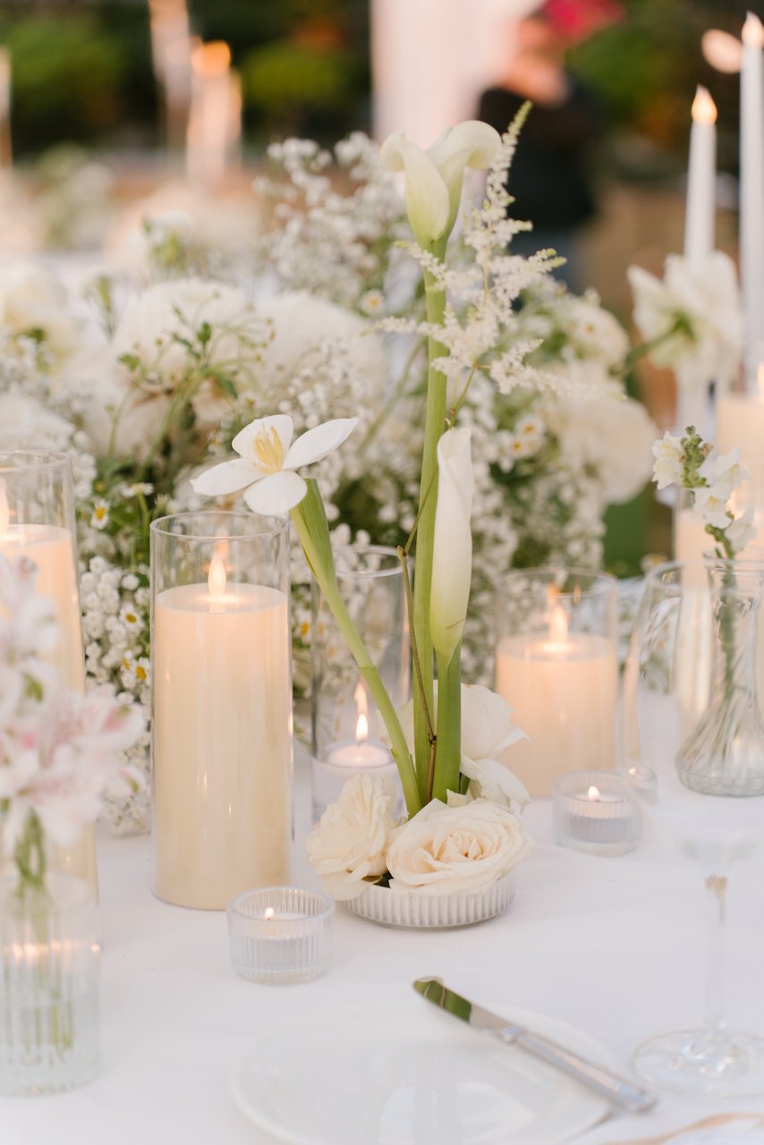 Elegant wedding table centerpiece with white orchids, roses, and glowing pillar candles