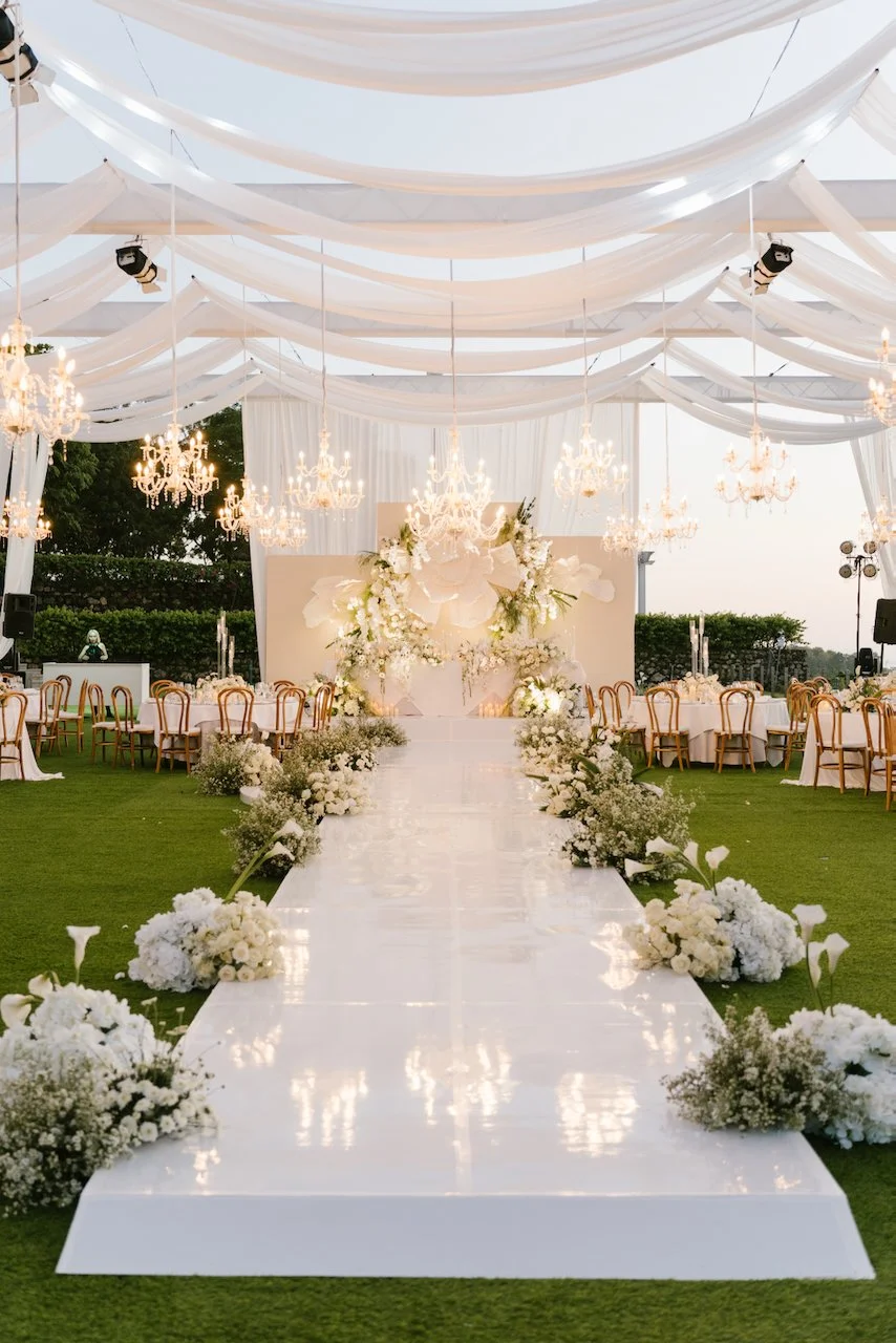 Luxury outdoor wedding reception setup at Ayana with a white aisle, drapery, and crystal chandeliers