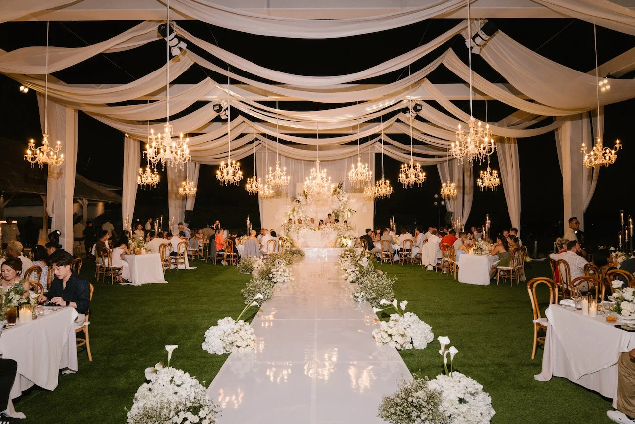 Wide evening view of the illuminated outdoor wedding reception canopy and dining tables