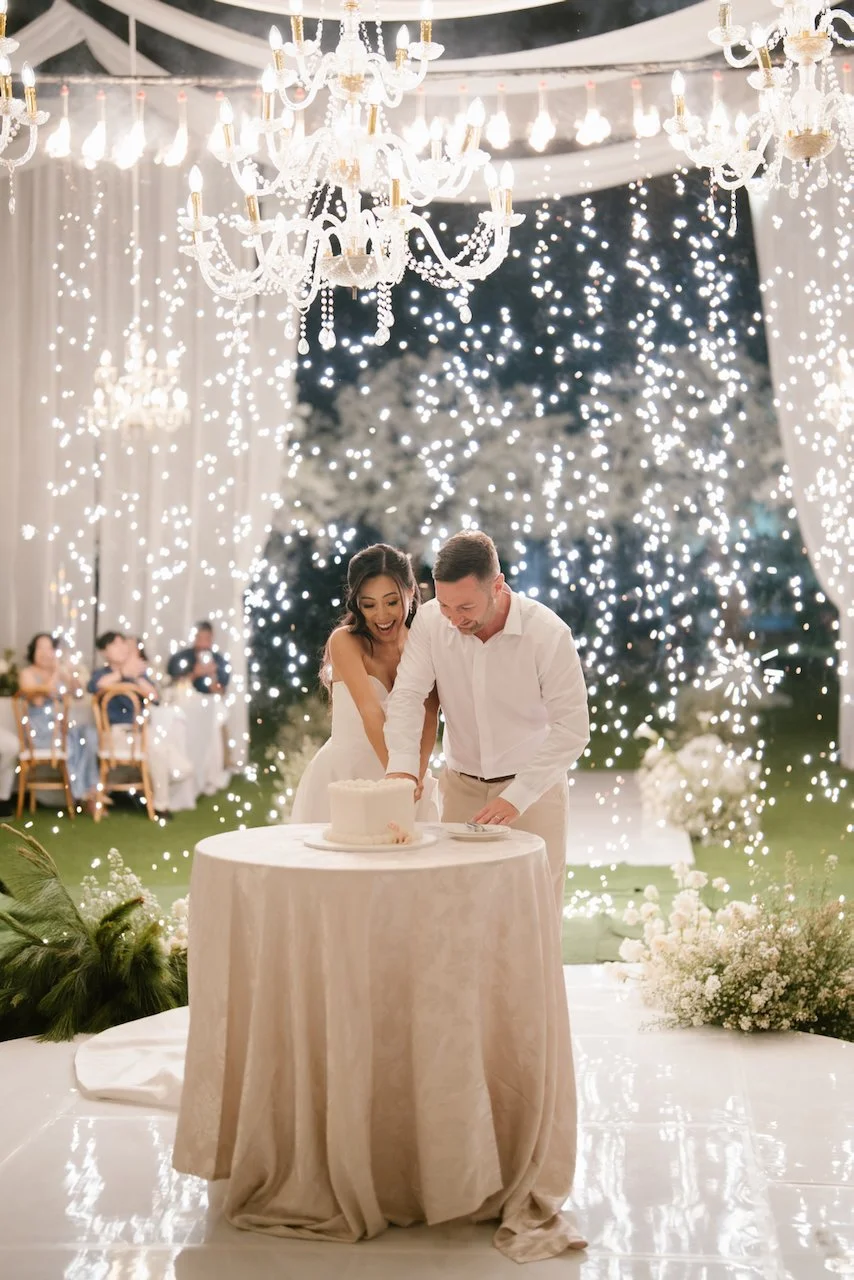 Bride and groom cutting their wedding cake under chandelier lighting and sparklers