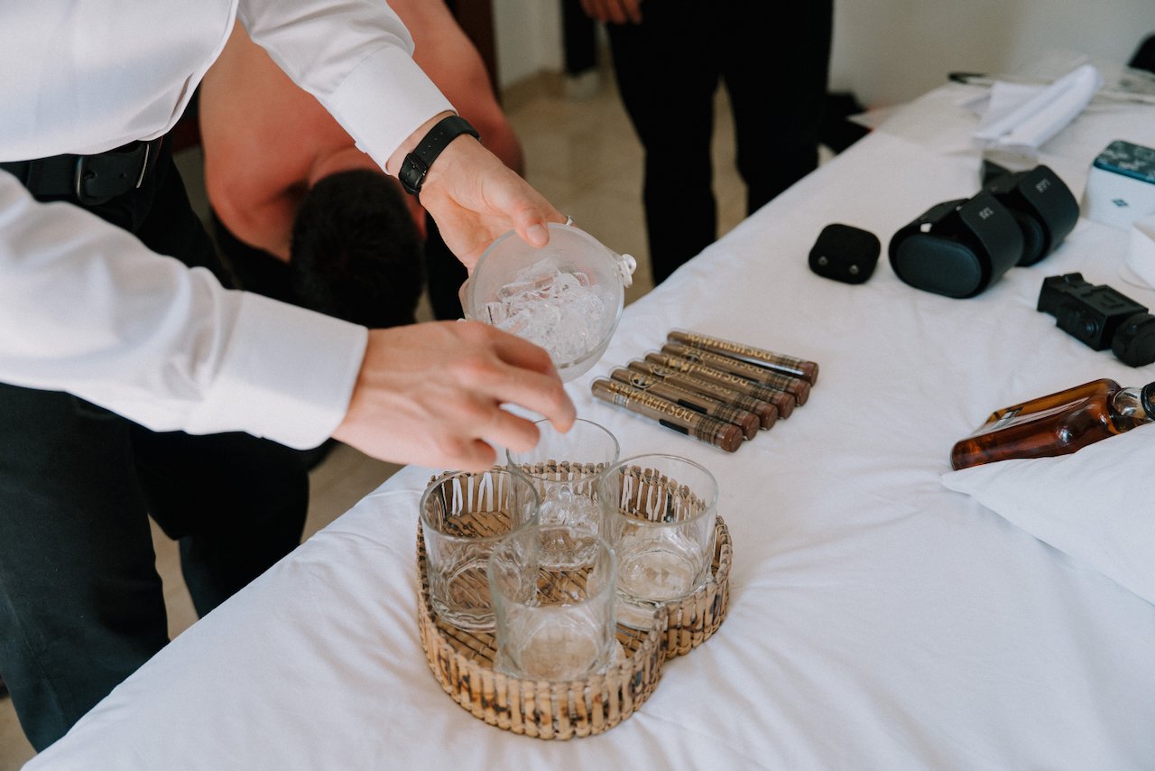 Groomsmen pouring drinks into glasses next to cigars before a Bali wedding