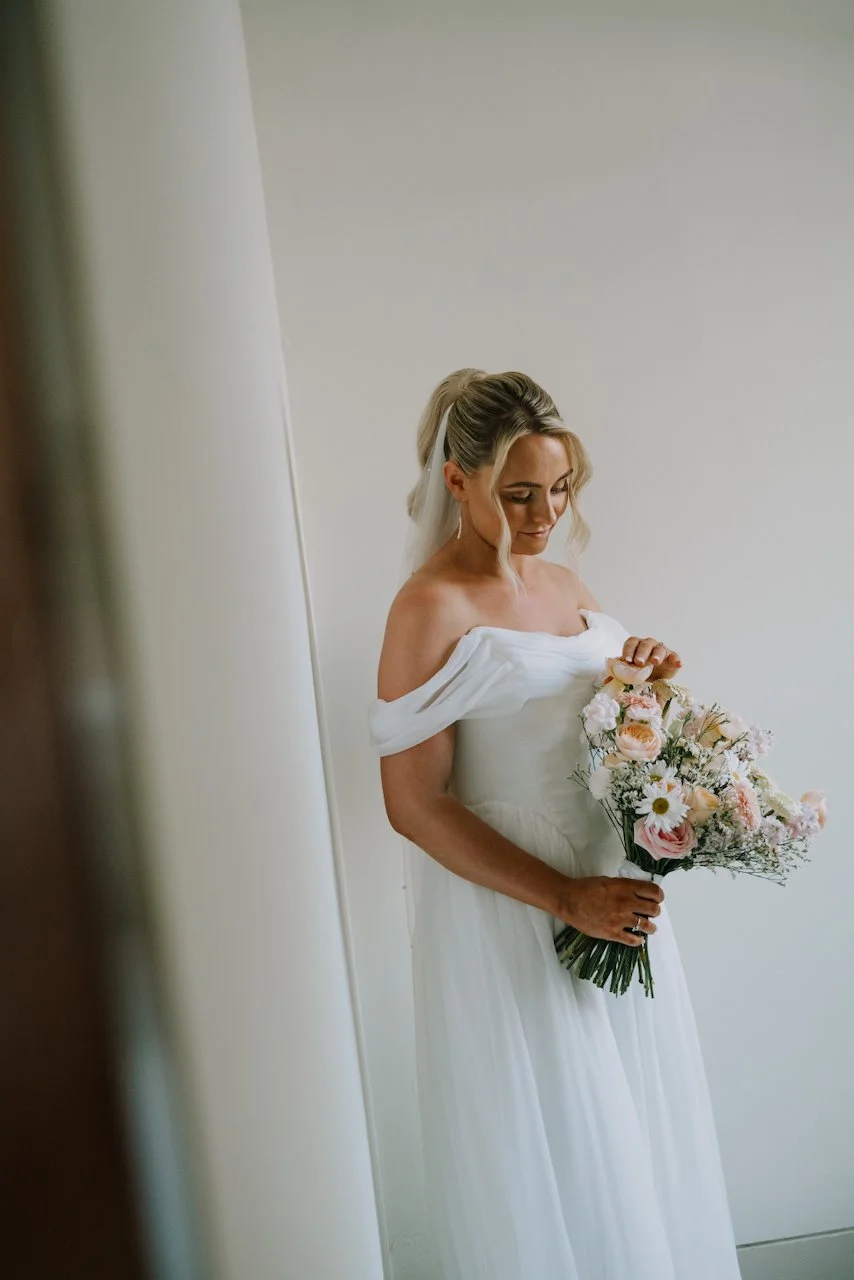 Bride Tegan holding a pastel floral bouquet in her white off shoulder wedding dress