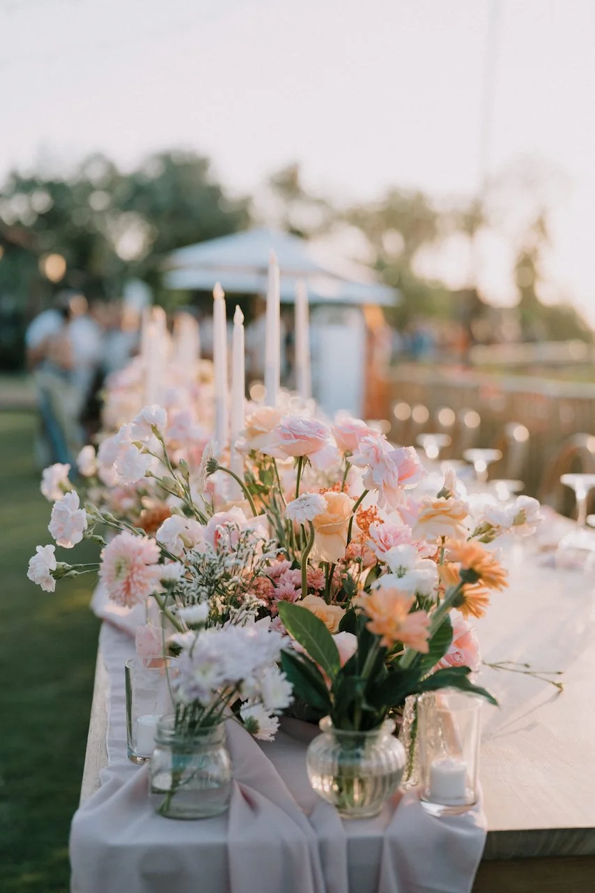 Long wooden reception table decorated with glowing candles and pastel floral centerpieces