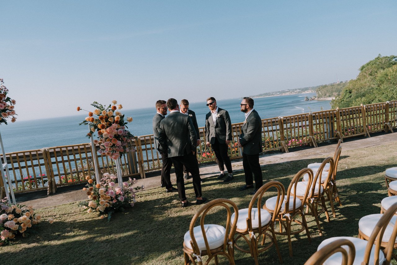 Groomsmen chatting on the sunny clifftop lawn overlooking the ocean at Uluwatu Cottages