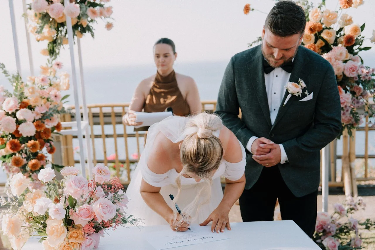Bride Tegan signing the wedding registry next to groom Liam at their clifftop ceremony
