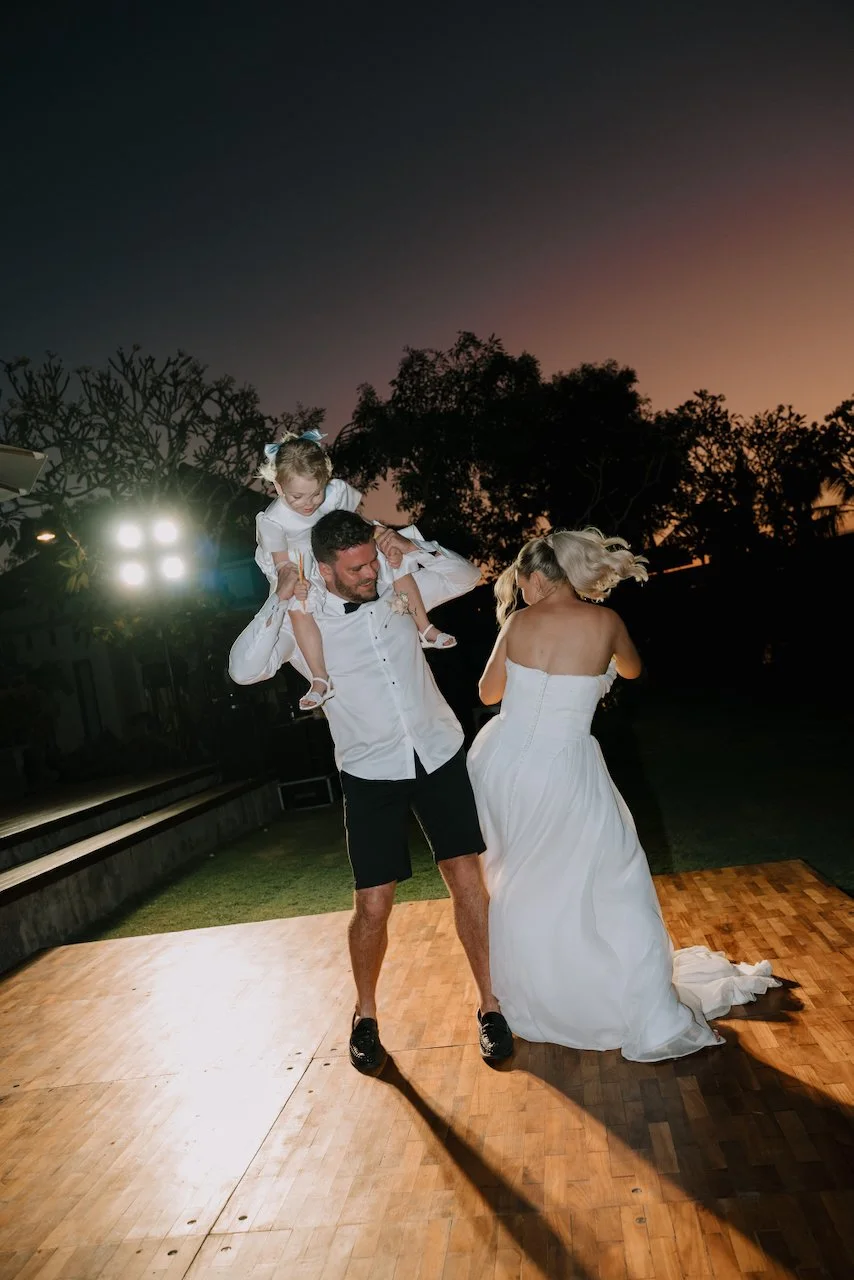 Groom dancing with a child on his shoulders while guests party around them