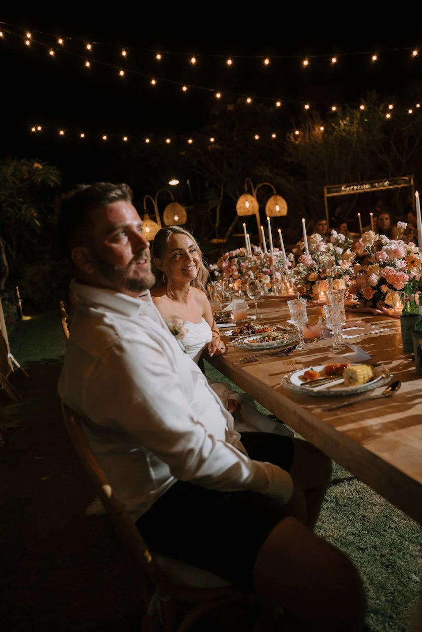 Newlyweds sitting at their candlelit reception table while guests give evening speeches