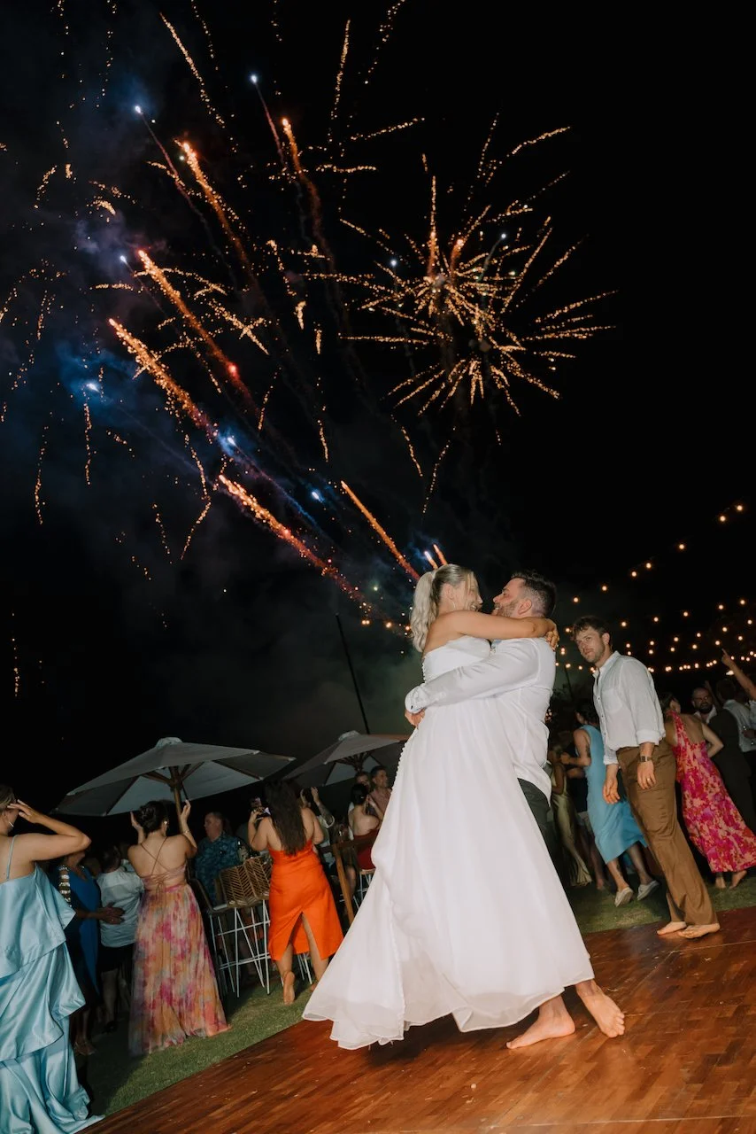 Tegan and Liam hugging while a vibrant fireworks display lights up the night sky
