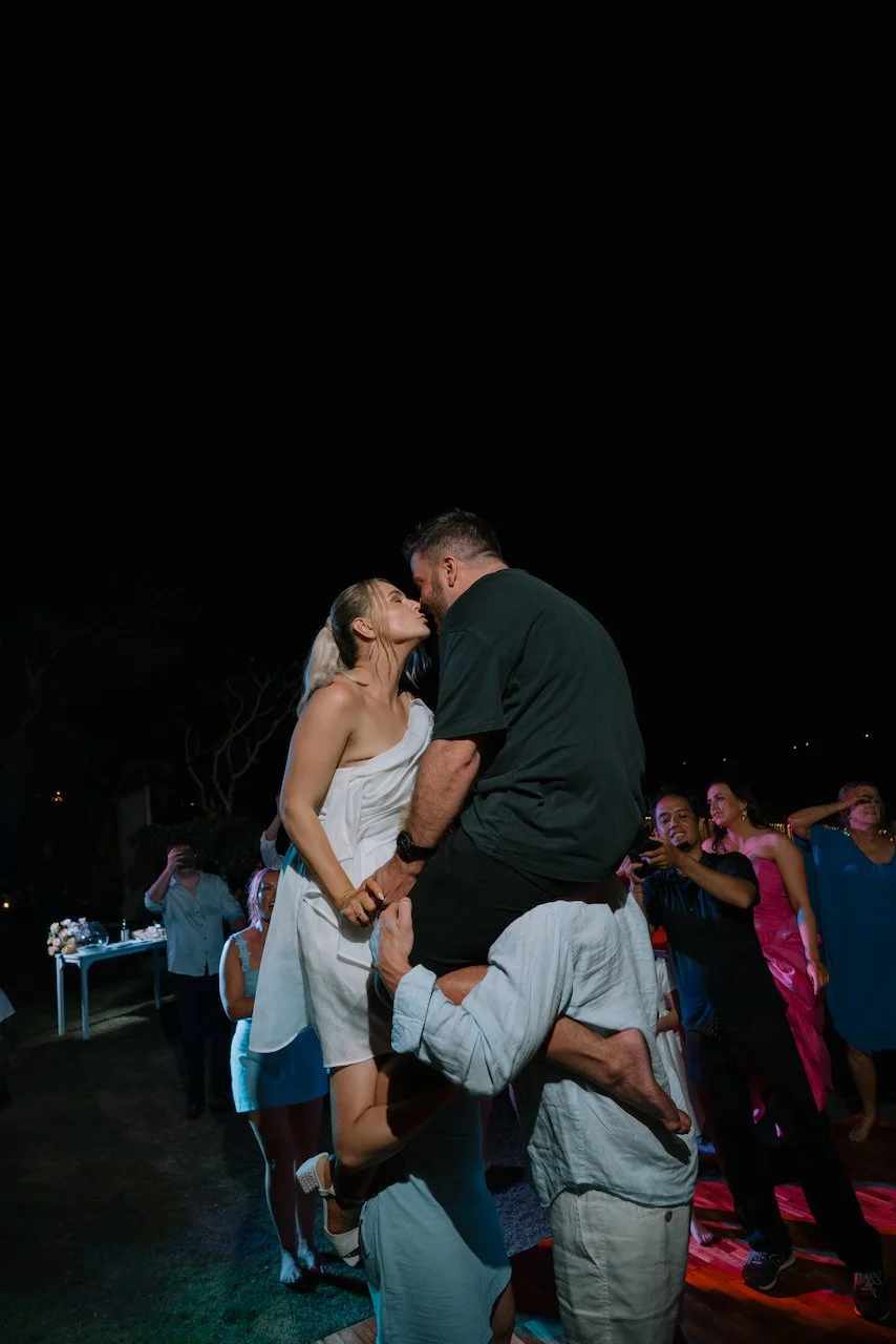 Tegan and Liam kissing while being held up on the shoulders of their friends on the dance floor