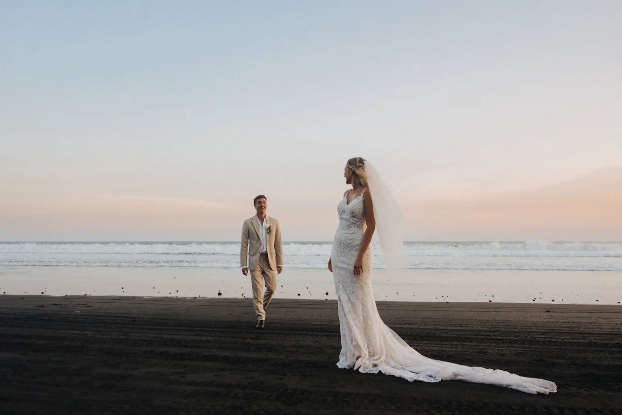 Devin and Daniella walking together along a sweeping black sand beach in Tabanan