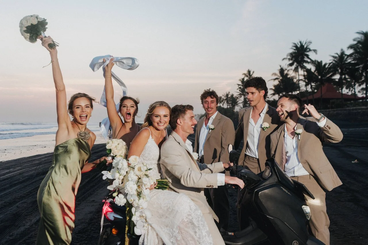 Bridal party having fun on the beach as groomsmen playfully carry the groom