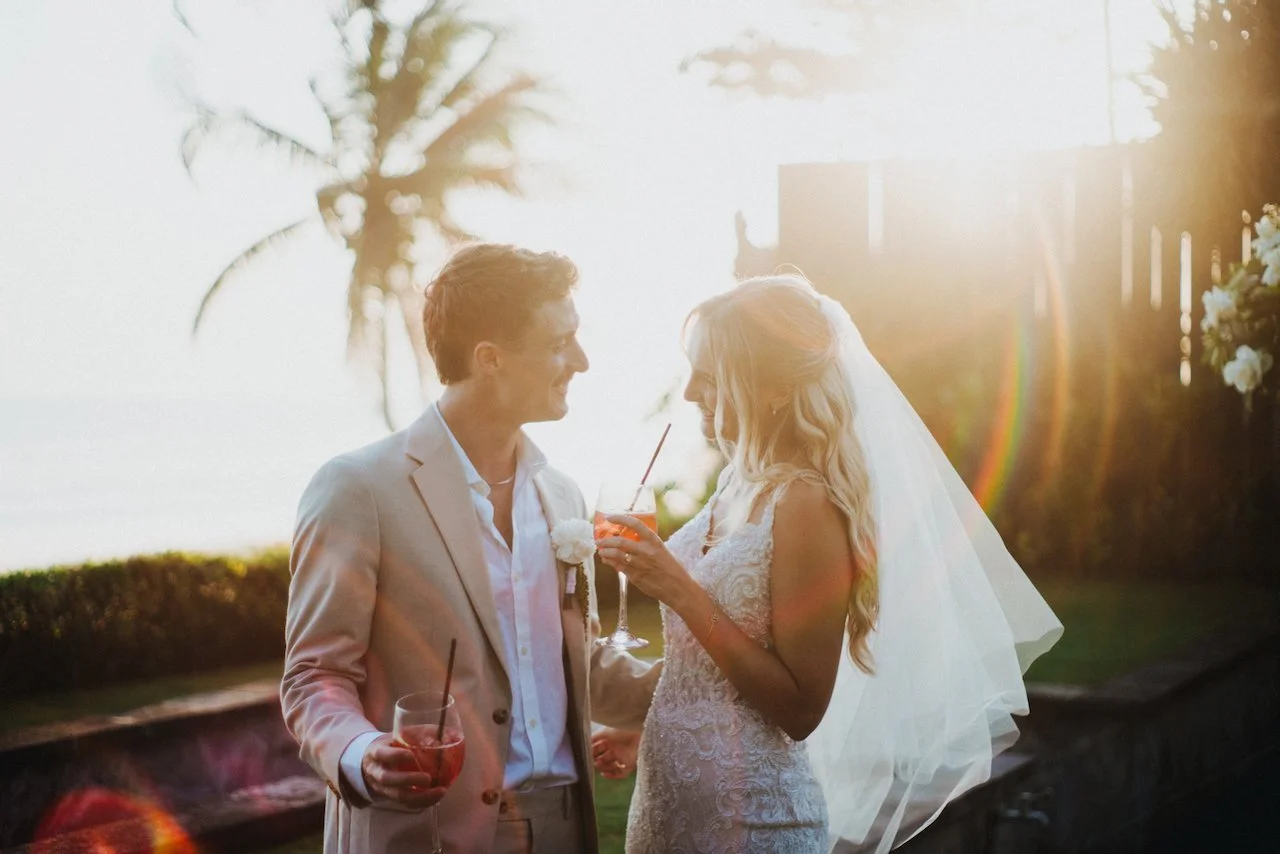 Newlyweds sharing a sunset toast with cocktails during their Bali destination wedding