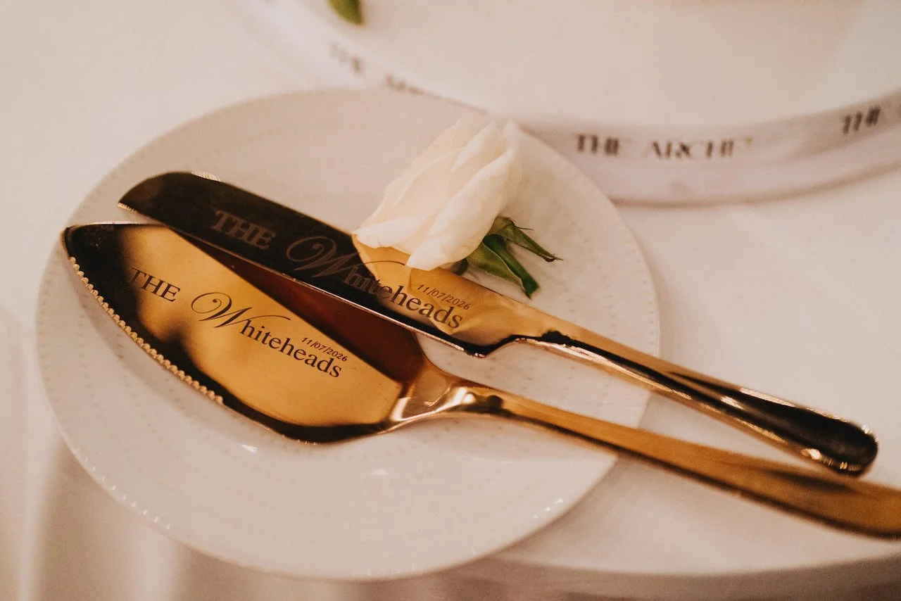 Custom gold cake cutting knives resting on a white plate with a single flower