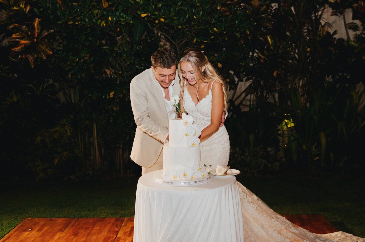 Devin and Daniella cutting their elegant white wedding cake in the tropical garden