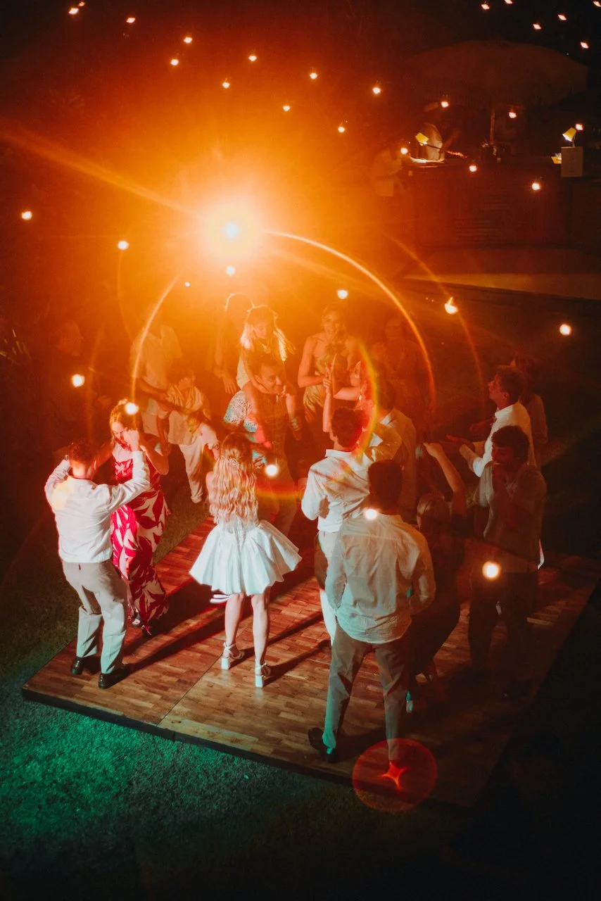 Wedding guests partying under warm string lights on an outdoor wooden dance floor