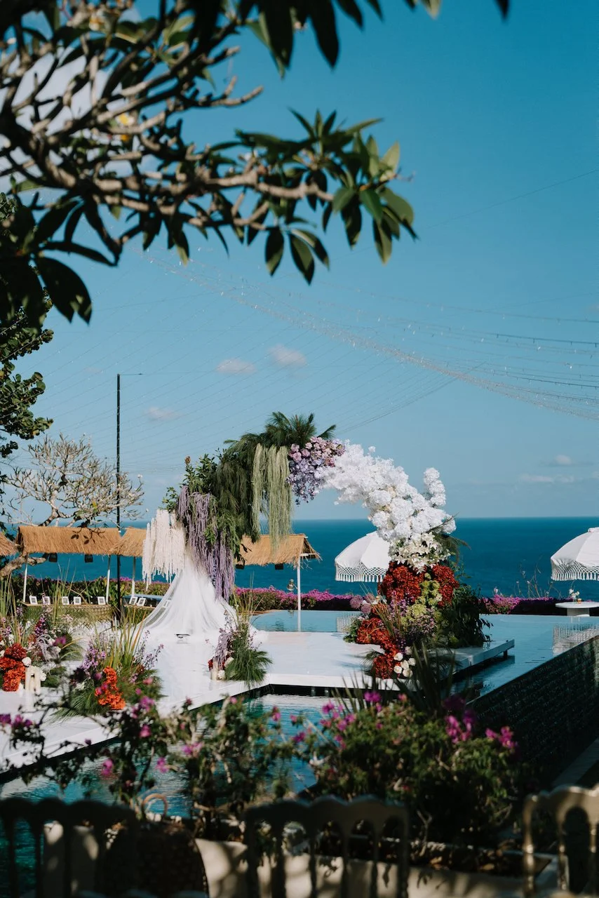 Clear acrylic wedding stage over an infinity pool with a colourful floral arch
