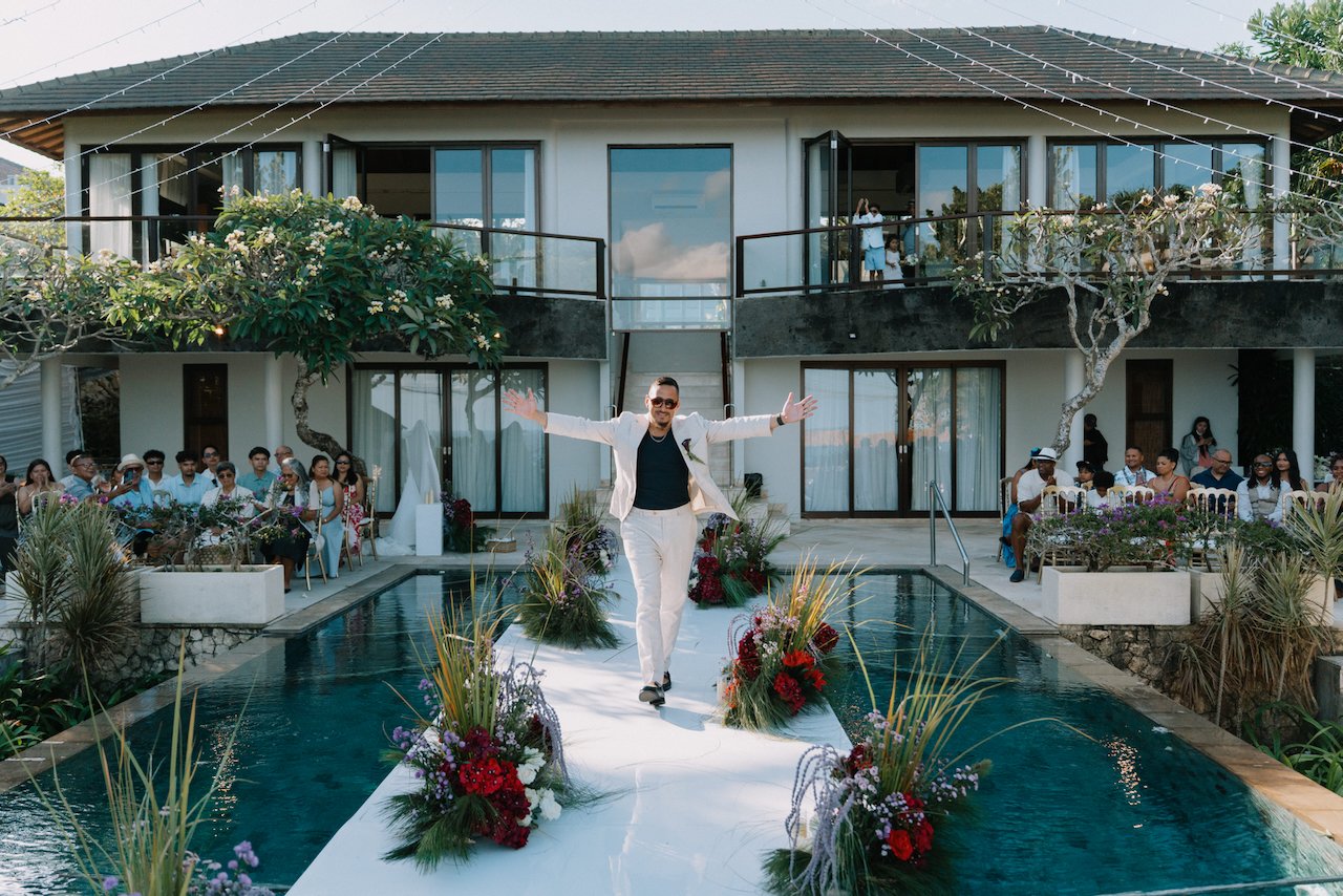 Groom walking down a clear aisle built over a pool for his vow renewal