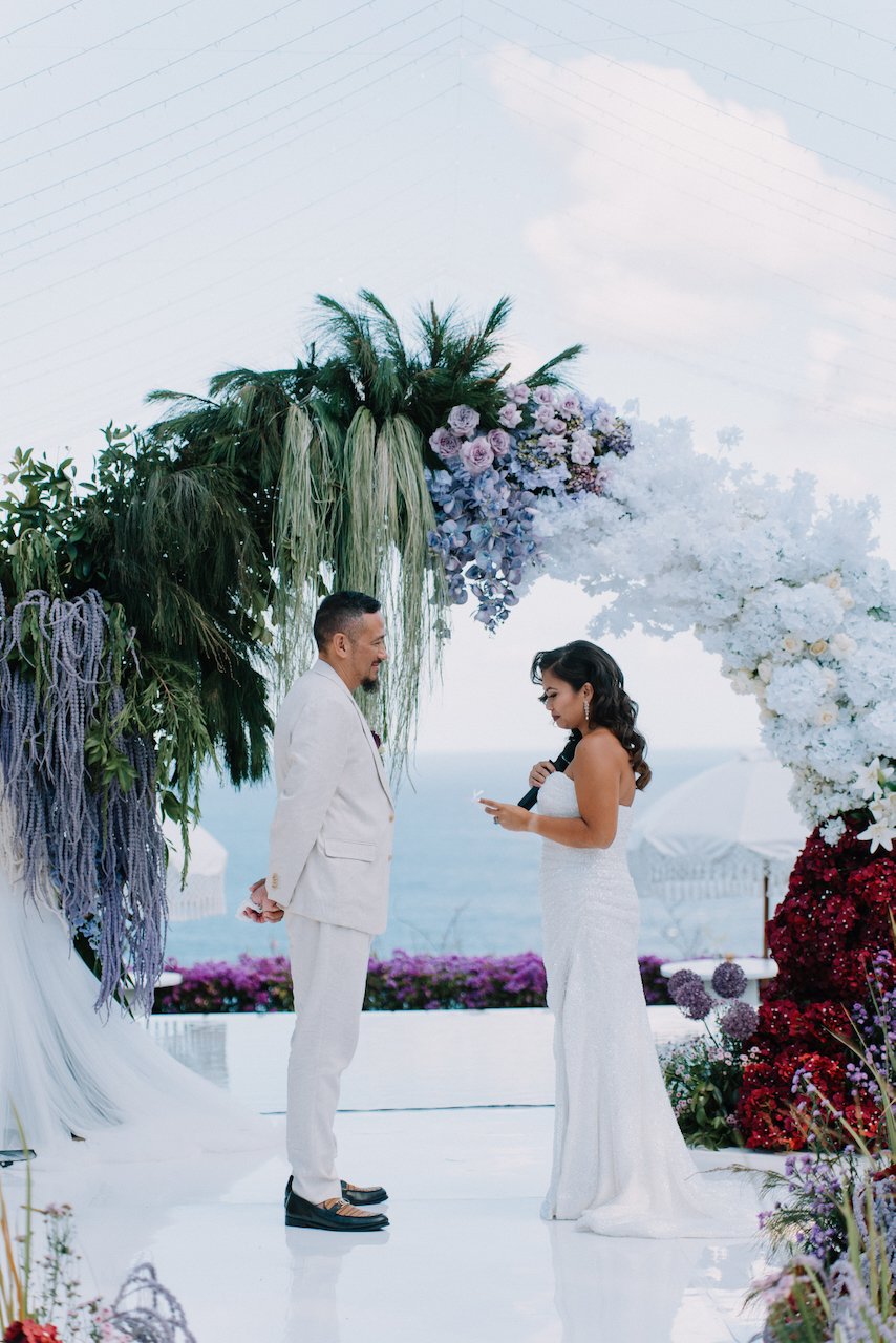 Michelle and John exchanging vows under a vibrant floral arch in Bali