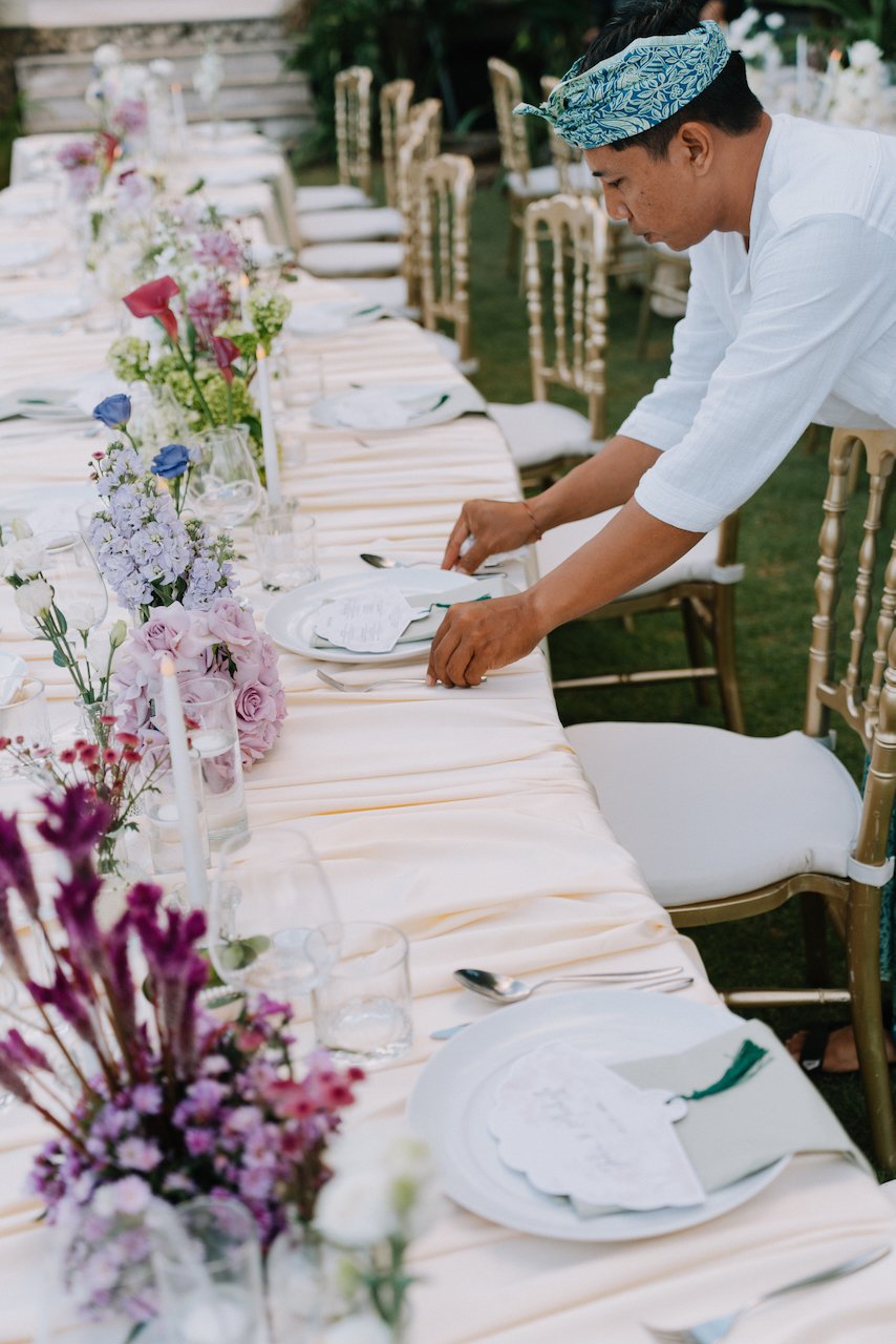 Staff setting a long banquet table with gold chairs for an outdoor reception