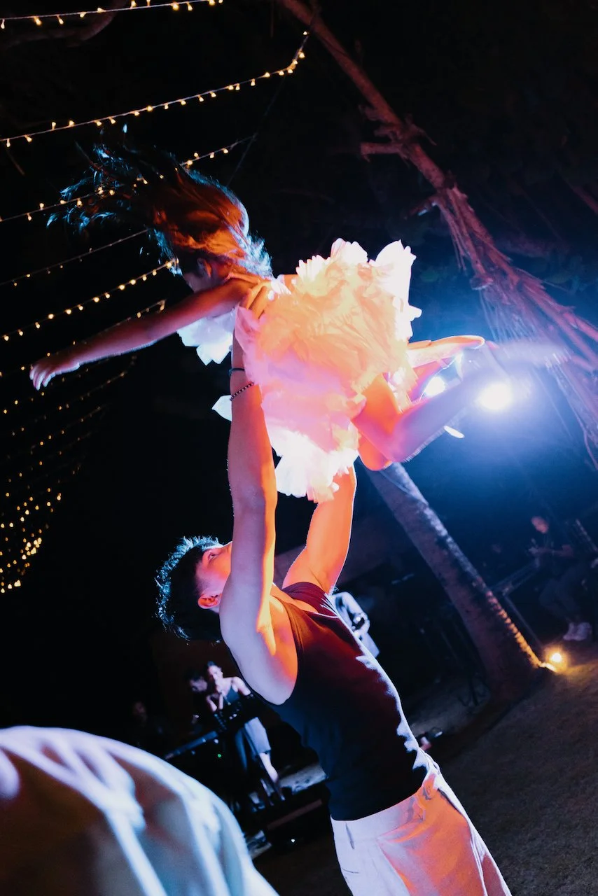 Sibling lifting a child on the outdoor dance floor under string lights