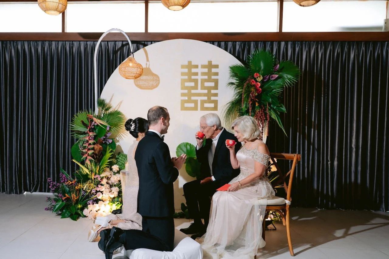 Bride and groom kneeling to serve tea to their parents at a Bali wedding tea ceremony
