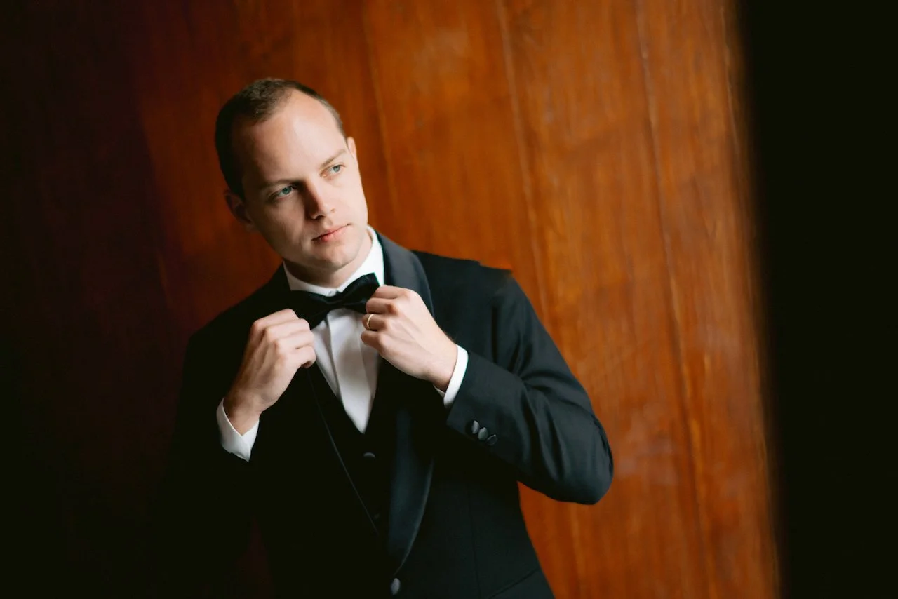 Groom Forrest adjusting his black bowtie while getting ready for his wedding day