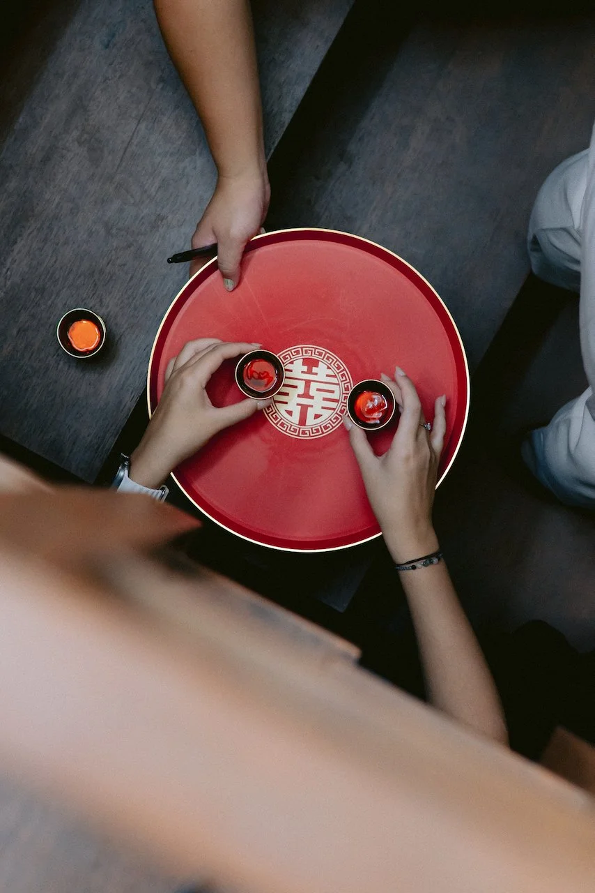 Overhead view of hands holding traditional red tea cups during a Chinese tea ceremony