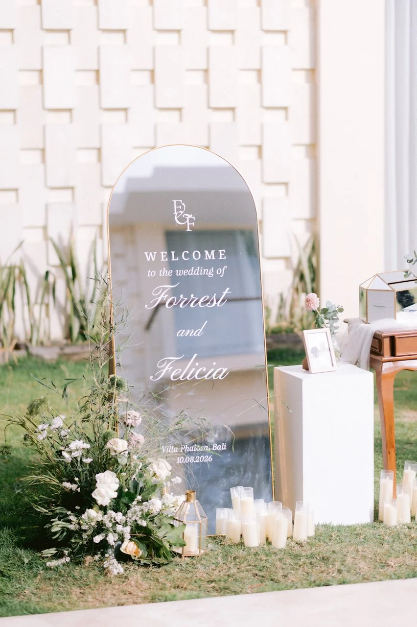 Mirror wedding welcome sign decorated with white flowers on a grassy lawn